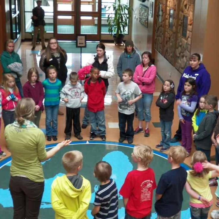 Elementary students and parents standing around a map of Michigan at GVSU's Lake Michigan Center.
